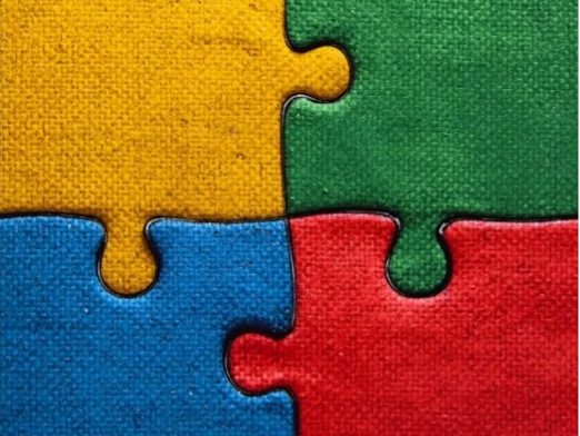 Quattro pezzi di puzzle colorati, giallo, verde, blu e rosso, incastrati tra loro.